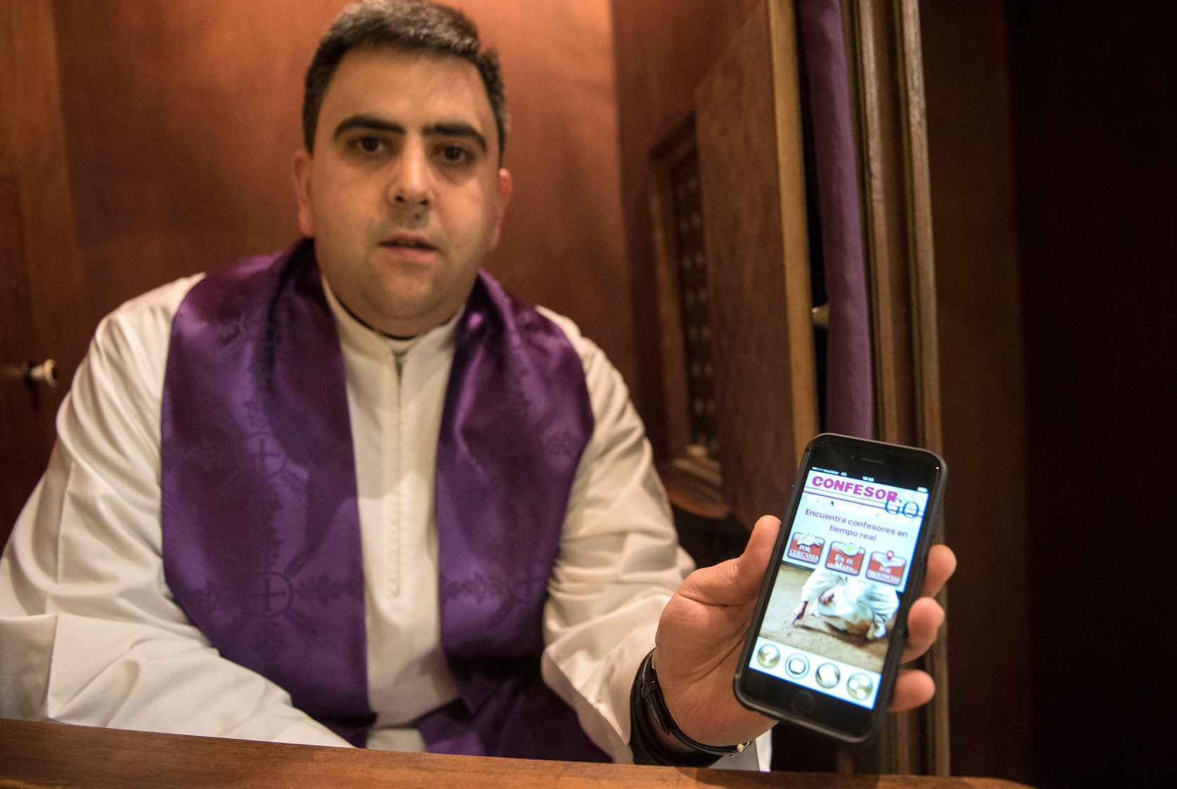 Mossèn Jordi Peña en un confessionari de l'església de Sant Celoni amb el mòbil i l'aplicació