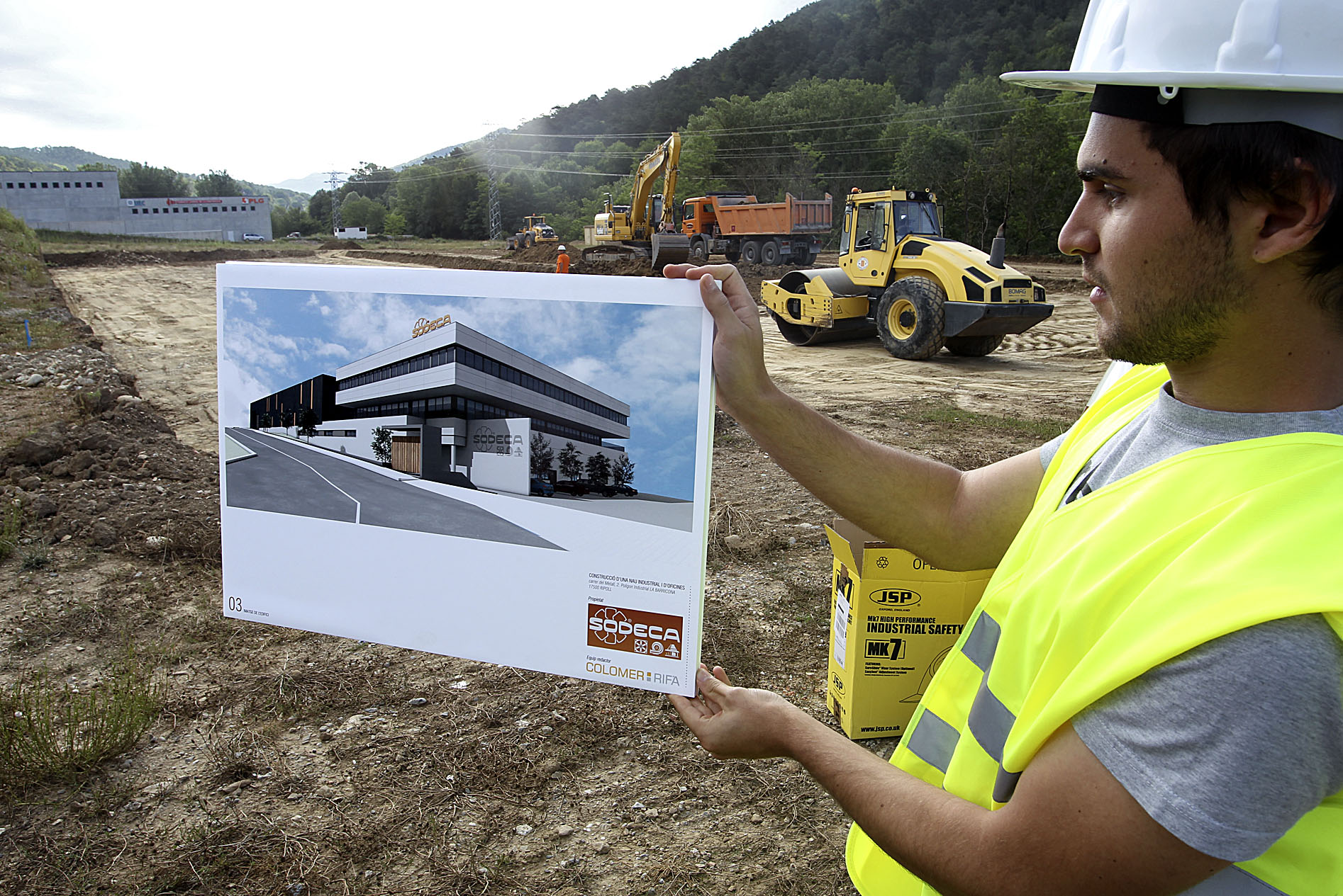 Un treballador mostrant com serà el nou edifici de Sodeca amb les obres al terreny comencades