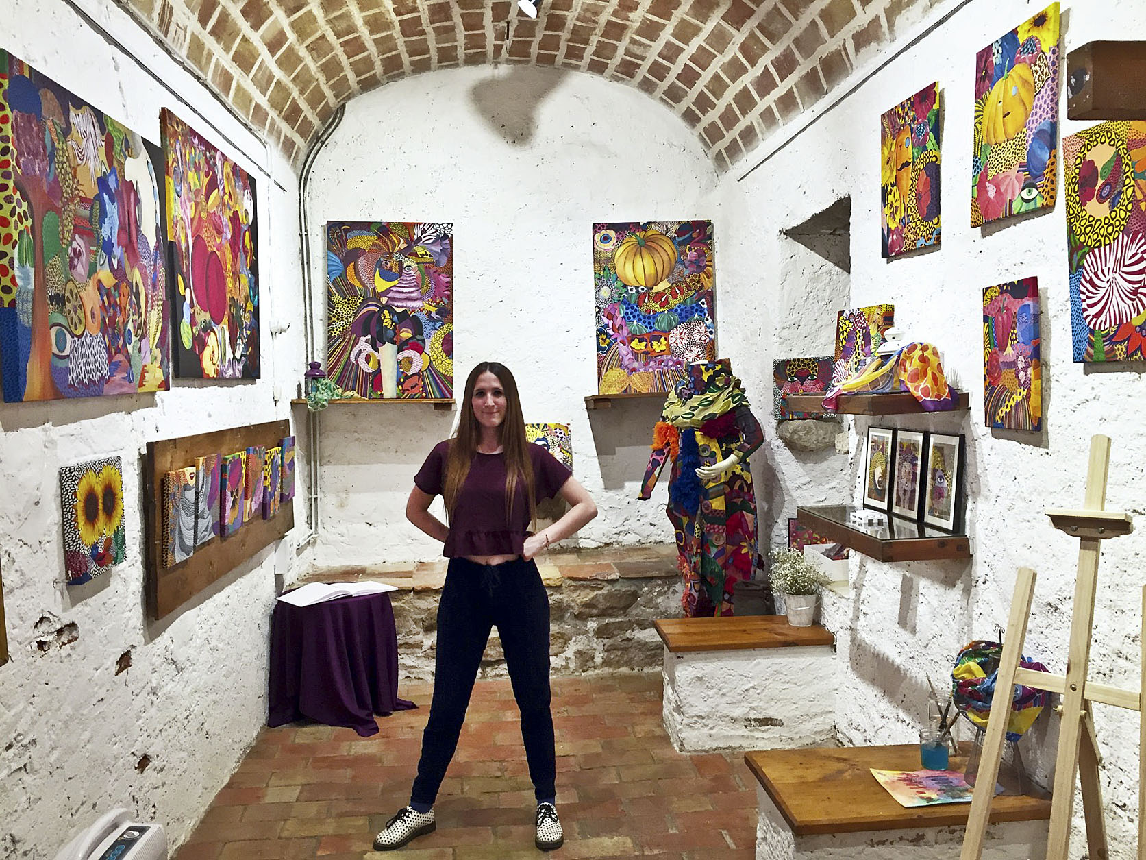 Anna Cortada juntament amb els seus quadres i la peça de roba 'Monster' en una exposició recent a Girona
