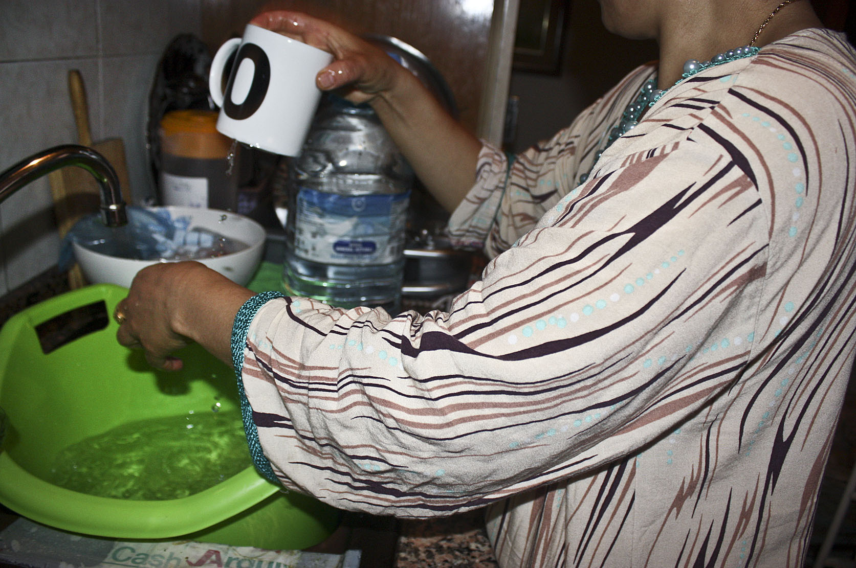 La veïna renta els plats amb l'aigua que puja en garrafes d'una font del carrer