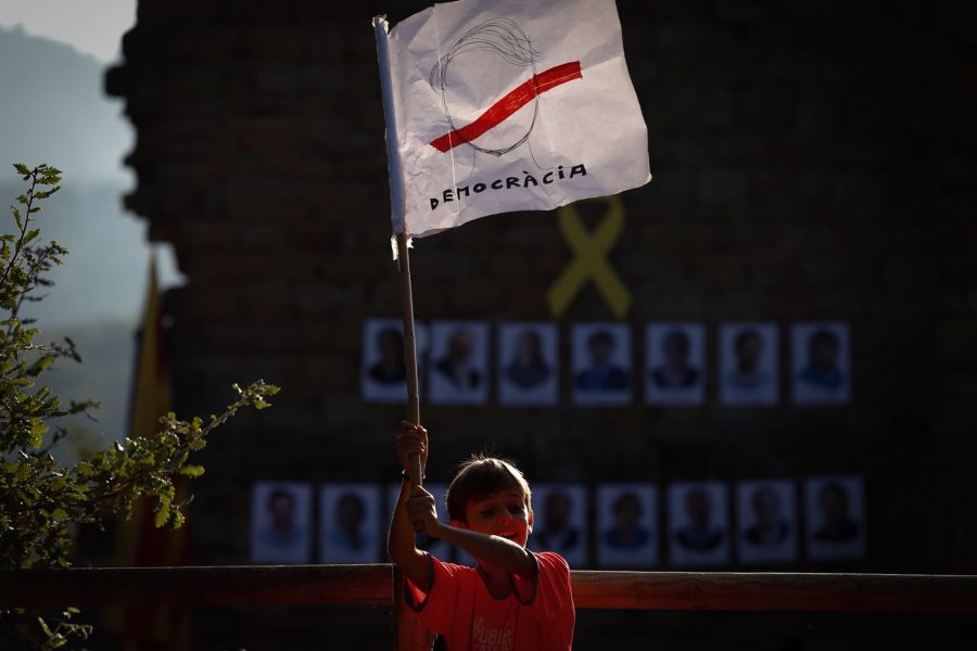 Un nen fent onejar la bandera de democràcia. Al darrere, les imatges dels presos polítics i exiliats