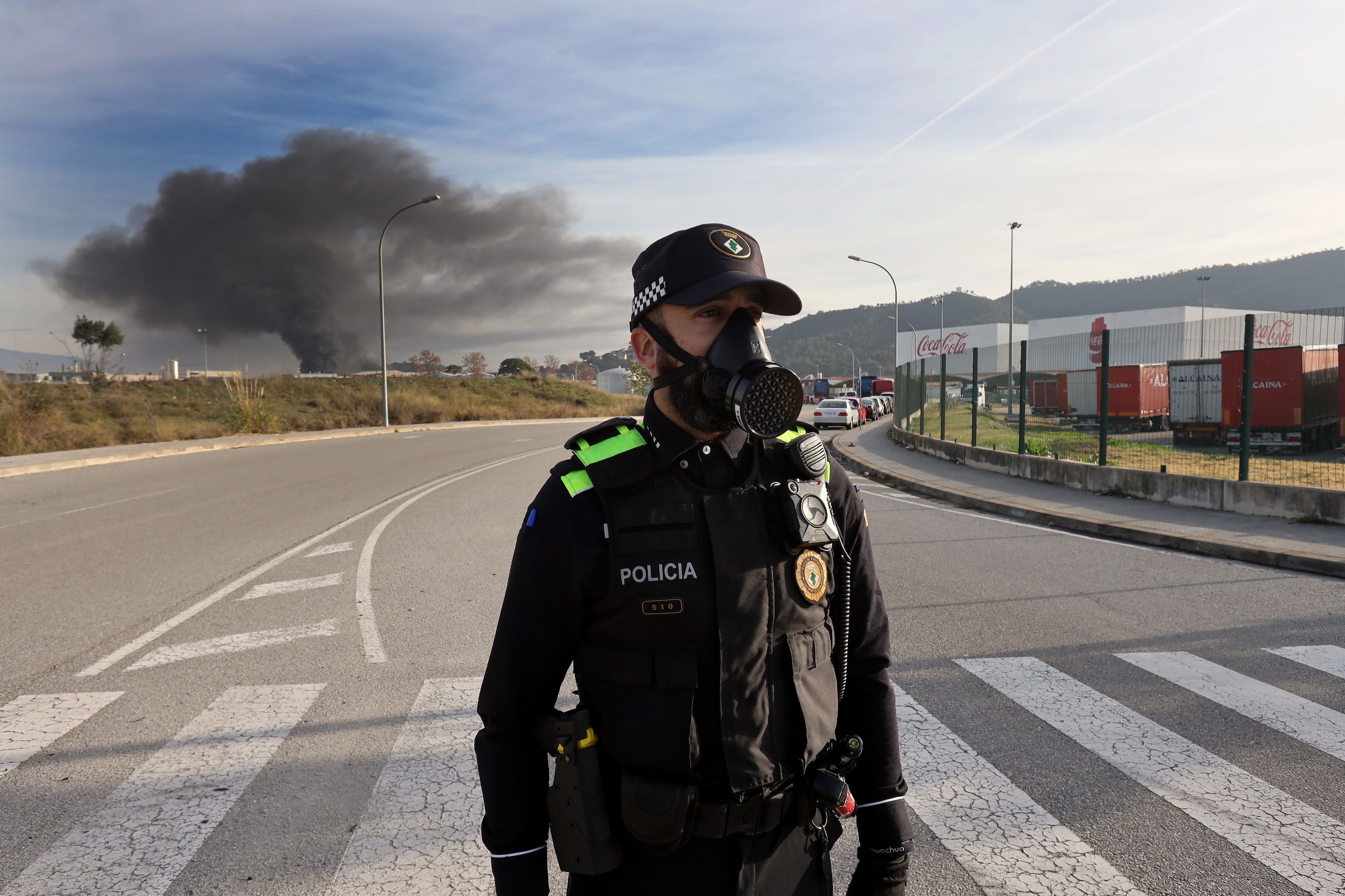 Un policia local amb mascareta amb la columna de fum al fons