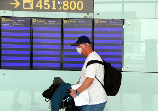 Un viatger amb mascareta passant per davant dels panells informatius de l'aeroport, sense cap vol
