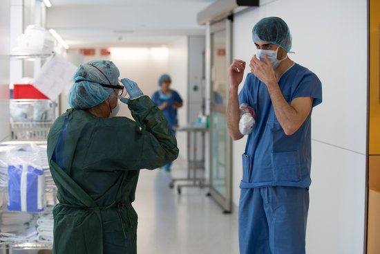 Un professional sanitari ajuda una companya a protegir-se abans d'atendre un pacient amb Covid-19