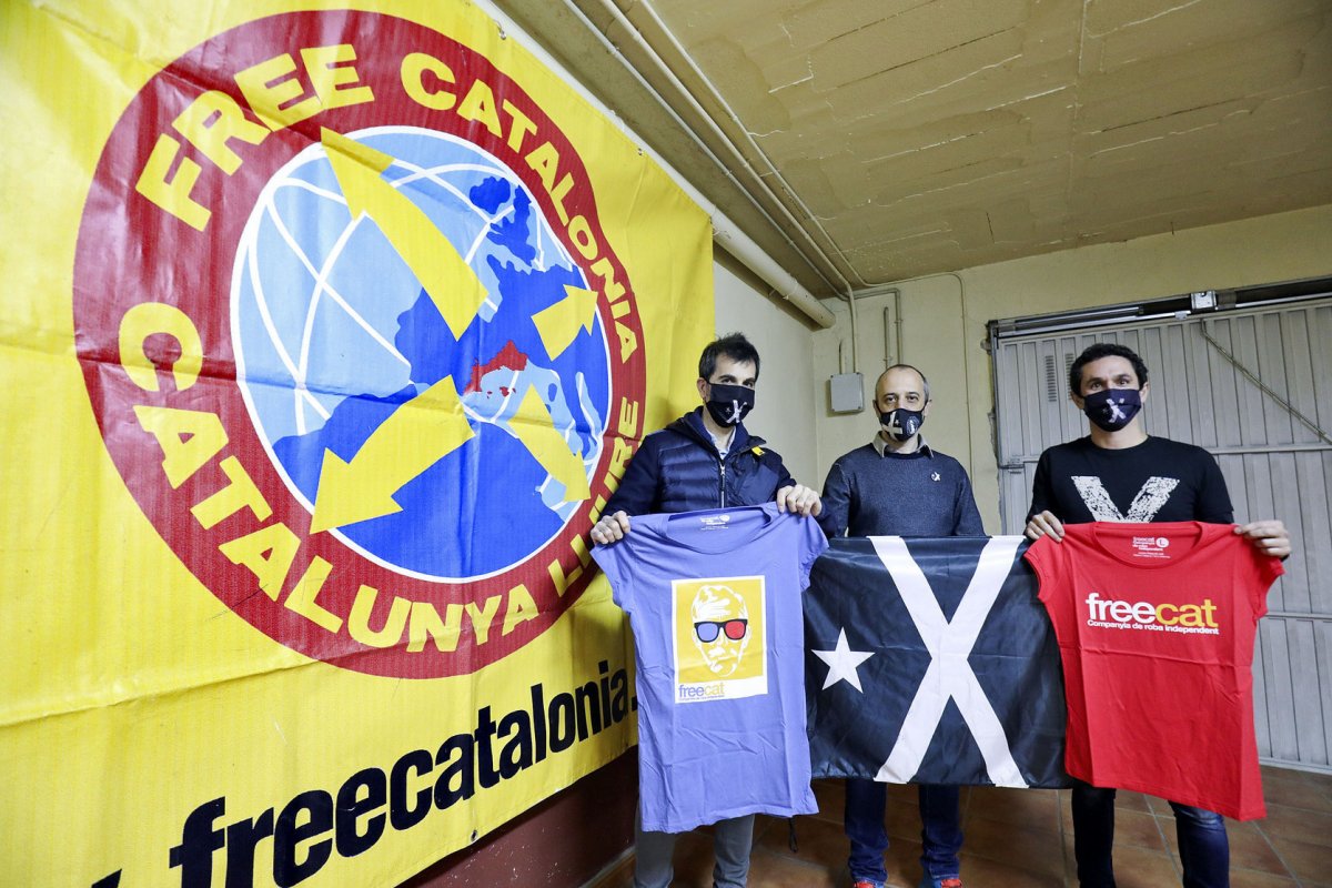 Oriol Folguera, Marc Sardà i Miquel Parareda, amb algunes de les samarretes i una estelada negra, davant de la pancarta de FreeCat