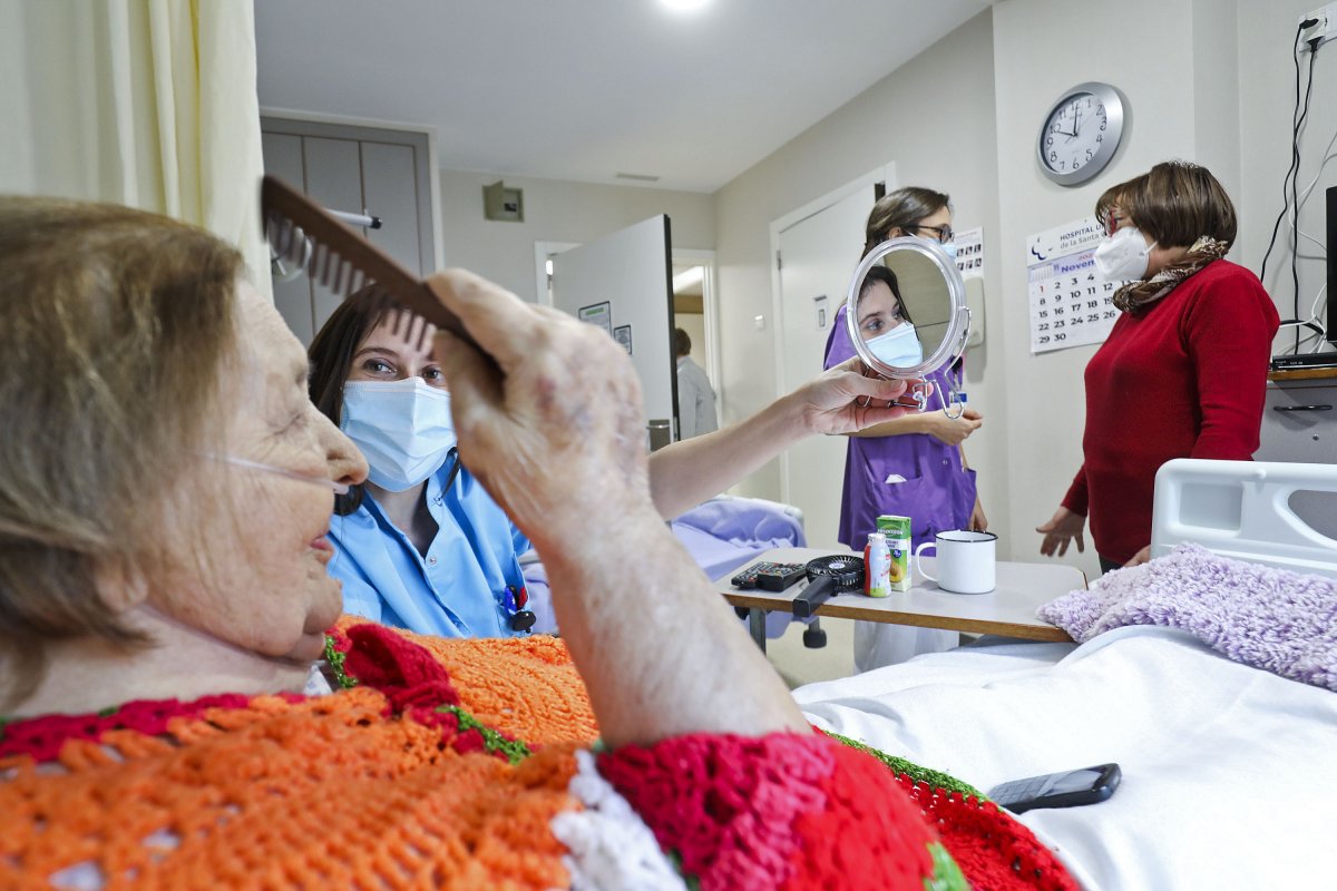 Antònia Muñoz es pentina gràcies a l'ajuda d'una infermera mentre una de les seves tres filles conversa amb una professional sanitària