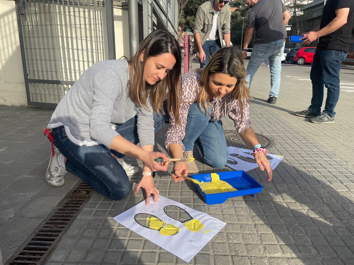 La directora de l'escola i la secretària de l'AFA pinten unes petjades a la porta del centre