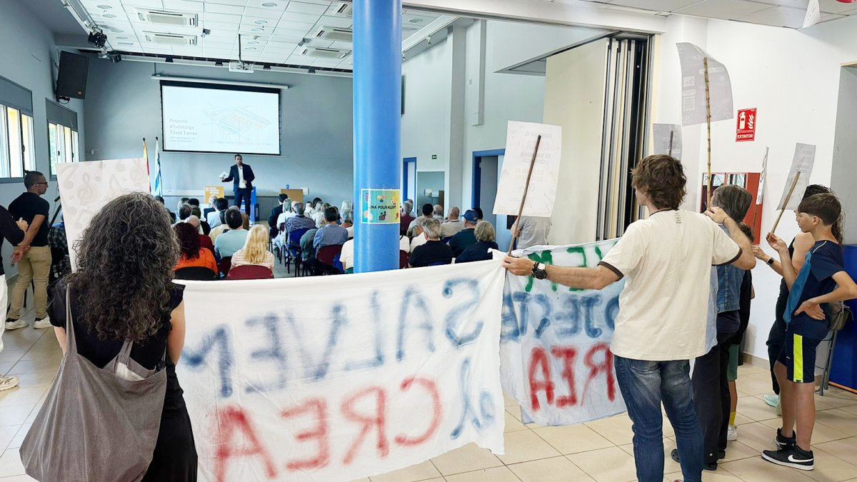 Un grup de manifestants va mostrar pancartes durant la intervenció de l’alcalde, al fons